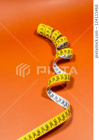 Tailor measuring tape in spiral rounds placed on orange surface Tailor measuring tape in spiral rounds placed on orange surface 124115468