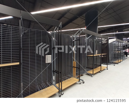 A row of empty metal retail shelves on wheels inside a modern store with black grid panels and overhead LED lighting. 124115595