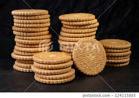 Stacks of round, golden-brown biscuits with a textured edge, arranged on a dark surface, creating a rustic and inviting bakery-style presentation Stacks of round, golden-brown biscuits with a textured edge, arranged on a dark surface, creating a rustic and inviting bakery-style presentation 124115885