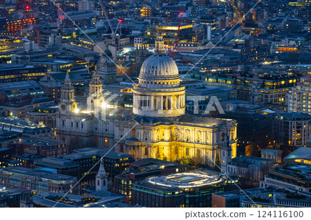 St Paul's Cathedral stands illuminated against the London skyline during evening hours. Surrounding buildings reflect city lights, showcasing a vibrant urban atmosphere. 124116100