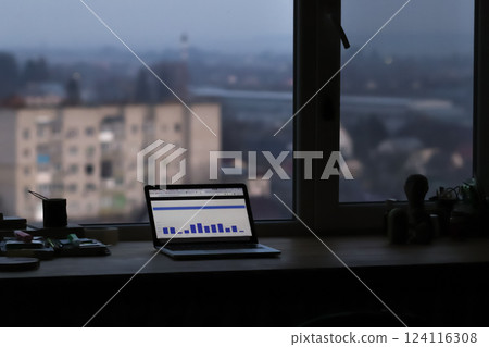 A laptop on an office desk near a window, displaying a diagram on its screen. The scene conveys a sense of productivity, business analysis, or late-night work 124116308