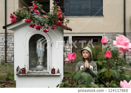 Child Praying Near Outdoor Shrine with Flower Decorations 124117868