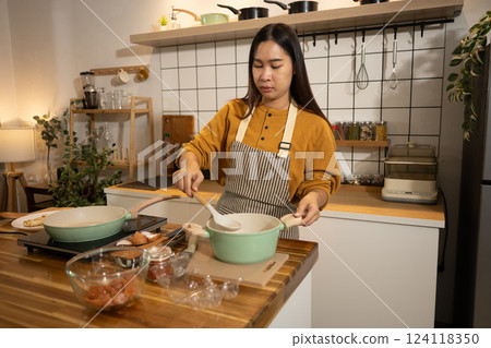 Young Asian woman wearing apron preparing meal in a warm kitchen 124118350
