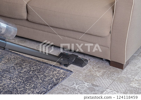 Modern upright cordless vacuum cleaner with dust light. Woman cleaning living room near sofa and carpet.  124118459