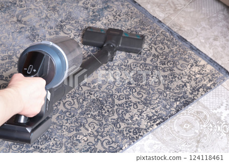 Modern upright cordless vacuum cleaner with dust light. Woman cleaning living room near sofa and carpet. Modern upright cordless vacuum cleaner with dust light. Woman cleaning living room near sofa and carpet. 124118461