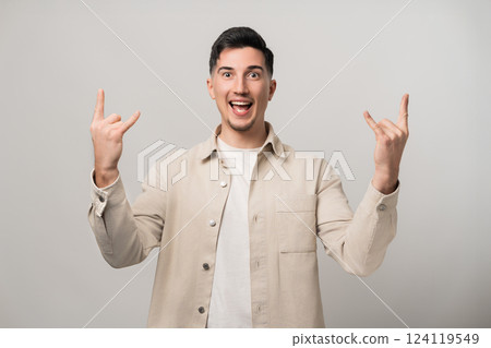 Let's rock it. Handsome brunette man in his 30s makes a cool rock sign with both hands, flashing a wide smile while looking into the camera. Trendy beige overshirt adds a modern touch Let's rock it. Handsome brunette man in his 30s makes a cool rock sign with both hands, flashing a wide smile while looking into the camera. Trendy beige overshirt adds a modern touch 124119549