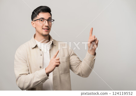 Handsome man in his 30s, wearing eyeglasses and a light beige overshirt, points upward and to the side with confidence. Ideal for promotional ads, marketing, and business presentations Handsome man in his 30s, wearing eyeglasses and a light beige overshirt, points upward and to the side with confidence. Ideal for promotional ads, marketing, and business presentations 124119552