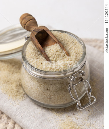 Glass jar of raw uncooked fonio seeds with a wooden scoop white table closeup. African cereal Glass jar of raw uncooked fonio seeds with a wooden scoop white table closeup. African cereal 124120244