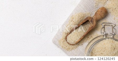 Raw uncooked fonio seeds in a wooden scoop near glass jar on white table top view. African cereal Raw uncooked fonio seeds in a wooden scoop near glass jar on white table top view. African cereal 124120245