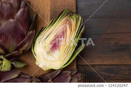 Half and whole purple raw roman artichokes on a dark wooden table top view. Fresh italian vegetables Half and whole purple raw roman artichokes on a dark wooden table top view. Fresh italian vegetables 124120247