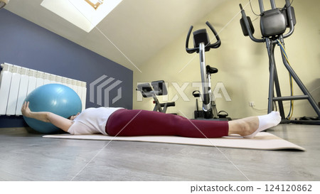 Woman in 50's doing pilates on fitness ball at home. Sports equipment and room for sports. Health and exercise. Woman in 50's doing pilates on fitness ball at home. Sports equipment and room for sports. Health and exercise. 124120862