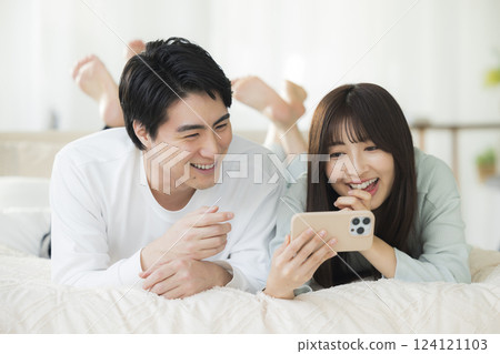 A young couple looking at a smartphone in bed 124121103