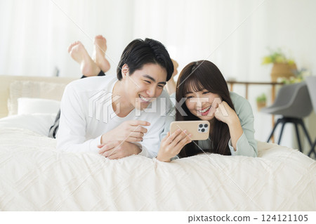 一對年輕夫婦在床上看智慧型手機 124121105