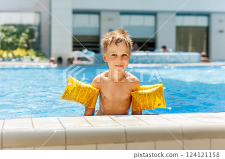 Portrait cute adorable little caucasian blond boy kid wear inflatable armband sit poolside indoor pool edge before swimming hotel spa thermal resort. Happy child enjoy summer vacation travel family Portrait cute adorable little caucasian blond boy kid wear inflatable armband sit poolside indoor pool edge before swimming hotel spa thermal resort. Happy child enjoy summer vacation travel family 124121158