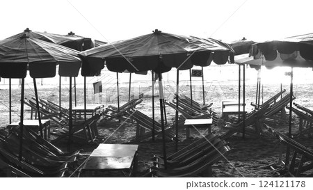 Black and white photo of a table and chairs on the beach. Black and white umbrellas with tables and chairs on the beach 124121178