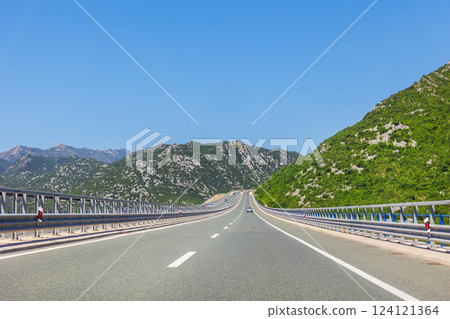 Open road leads between green mountains under bright sky. This sunny highway in Croatia captures freedom and scenic drive across a lush Mediterranean landscape, inviting endless exploration 124121364