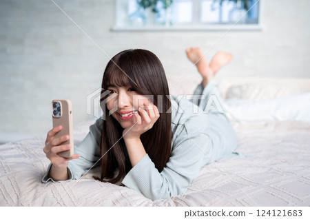 A woman lying face down looking at her smartphone A woman lying face down looking at her smartphone 124121683