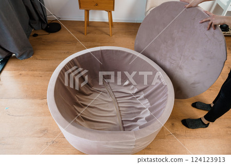 Person Assembling a Modern, Round, Velvet Upholstered Furniture Piece with Removable Cushioned Seat Indoors 124123913