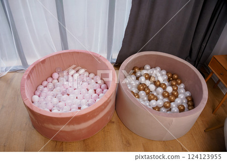 Two Round Pink and Beige Soft Ball Pits Filled with Pink, White, Gold, and Transparent Plastic Balls Near Curtains in Stylish Room Two Round Pink and Beige Soft Ball Pits Filled with Pink, White, Gold, and Transparent Plastic Balls Near Curtains in Stylish Room 124123955