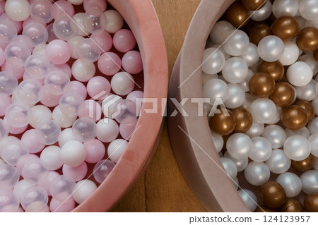 Close-up of Two Colorful Ball Pits Filled With Pink, White, and Bronze Plastic Balls on Wooden Floor Close-up of Two Colorful Ball Pits Filled With Pink, White, and Bronze Plastic Balls on Wooden Floor 124123957