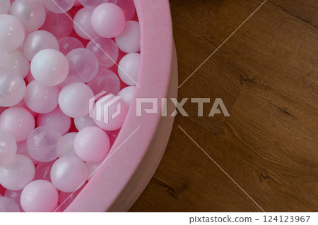 Pink and White Plastic Balls in Soft Pink Play Pit on Wooden Floor Background 124123967