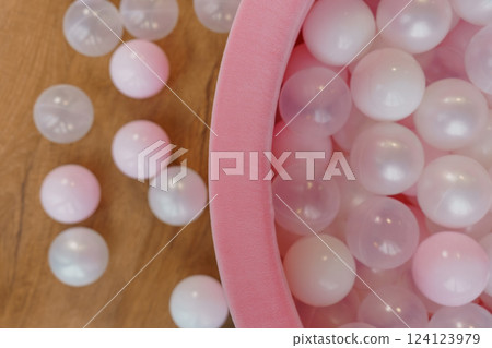 Close-up of Pink and White Plastic Balls in Soft Pink Container with Several Balls Scattered on Wooden Floor 124123979