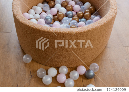 Soft Brown Play Ball Pit Filled with Pastel and Neutral Colored Plastic Balls on Wooden Floor 124124009