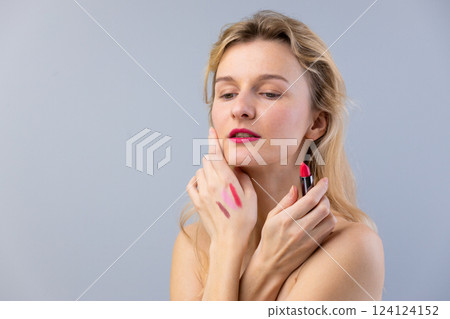 Exploring the Art of Makeup: A Woman Testing Lipstick Shades with Grace and Elegance Against a Soft Gray Background, Perfect for Beauty Inspiration 124124152