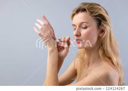 A Young Woman Applying Makeup to Her Arm While Looking Thoughtfully Off-Camera, Capturing the Artistry of Beauty and Self-Expression in a Minimalist Setting A Young Woman Applying Makeup to Her Arm While Looking Thoughtfully Off-Camera, Capturing the Artistry of Beauty and Self-Expression in a Minimalist Setting 124124267