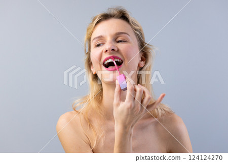 Woman Applying Glossy Lip Color with a Smile, Emphasizing Beauty and Confidence in a Minimalist Studio Background for Captivating Visual Appeal Woman Applying Glossy Lip Color with a Smile, Emphasizing Beauty and Confidence in a Minimalist Studio Background for Captivating Visual Appeal 124124270