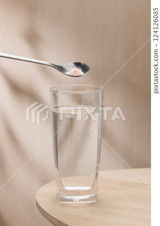A spoon of Himalayan salt is being added to a glass of drinking water. 124126085