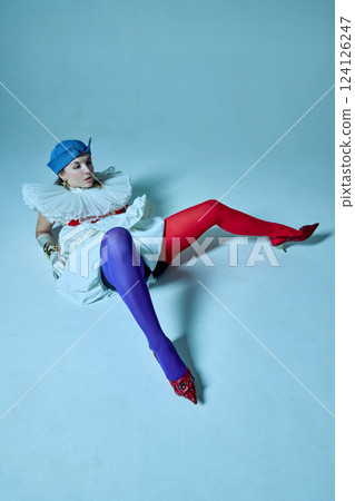 Woman in striking red and blue tights lies on floor with legs wide apart, against studio background. View from above. Woman in striking red and blue tights lies on floor with legs wide apart, against studio background. View from above. 124126247