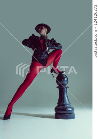 Woman in bold red tights and black stylish outfit standing atop chess piece, gazing confidently. Concept of fashion Woman in bold red tights and black stylish outfit standing atop chess piece, gazing confidently. Concept of fashion 124126272