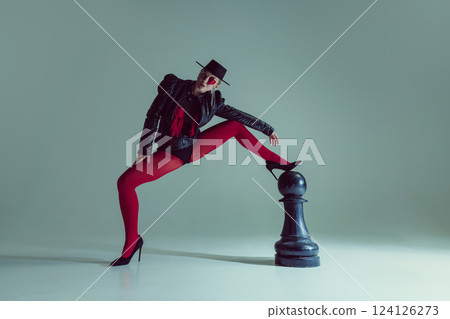Woman in gothic fashion and surreal styling reclines on chess piece, transforming game into artful abstraction. Concept of beauty, fashion. 124126273