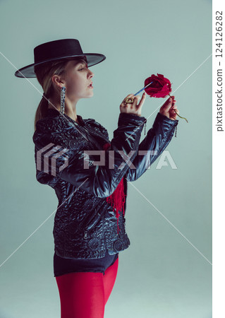 Mystical woman in wide-brimmed hat carefully painting red rose with brush against soft background. Concept of art Mystical woman in wide-brimmed hat carefully painting red rose with brush against soft background. Concept of art 124126282