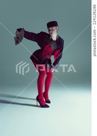 Young woman in black tailored jacket, red tights, and heels crouching while extending cards. Concept of fashion, strategy Young woman in black tailored jacket, red tights, and heels crouching while extending cards. Concept of fashion, strategy 124126286
