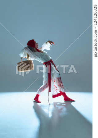 Expressive young woman in white-red outfit, bending backward with basket, embodying movement as storytelling, symbolizing transformation and inner conflict. 124126329