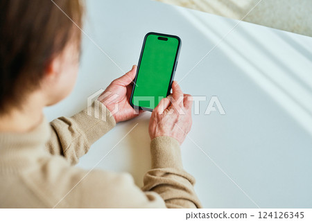 Senior woman operating a smartphone Green background 124126345