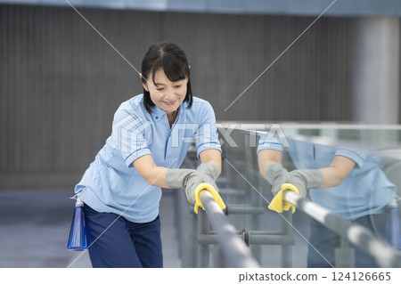 Image of building cleaning: A female cleaning staff member in her 50s wiping the handrails in the hallway 124126665