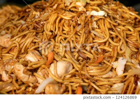 Street food festival in Europe. Asian fast food at market stall. Close-up of stir-fried chicken and vegetables noodles. Fresh, flavorful, authentic taste of street cuisine. Street food festival in Europe. Asian fast food at market stall. Close-up of stir-fried chicken and vegetables noodles. Fresh, flavorful, authentic taste of street cuisine. 124126869