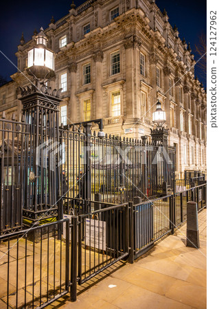 The security gate of Downing Street stands tall at night, surrounded by the elegant architecture of Westminster. Soft lights cast a warm glow, highlighting this historic landmark in London. The security gate of Downing Street stands tall at night, surrounded by the elegant architecture of Westminster. Soft lights cast a warm glow, highlighting this historic landmark in London. 124127962