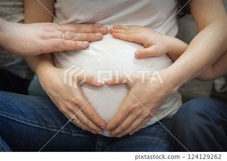 a pregnant woman in a white T-shirt and blue jeans. Close-up of the baby. Dad and mom's hands. Ivf, family, love, family planning, gynecologist, doctor, children. High quality photo 124129262