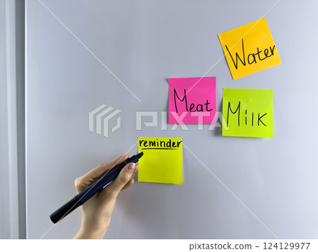 Hand writing note on colored reminder hanging on refrigerator 124129977
