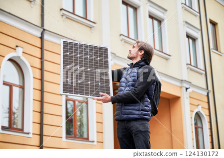 Man holding photovoltaic solar panel in front of historical building. Concept of integration of sustainable renewable energy sources into architecture. 124130172