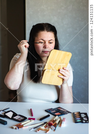 Vertical image of Millennial Caucasian woman doing self make up applying mascara while looking in mirror. Getting ready. Beauty concept. Vertical image of Millennial Caucasian woman doing self make up applying mascara while looking in mirror. Getting ready. Beauty concept. 124131135