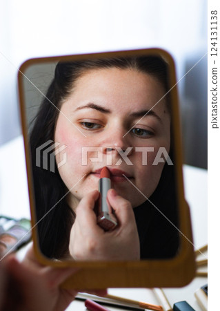 Vertical image of Millennial Caucasian woman doing self make up applying lipstick to lips while looking in mirror. Reflection in mirror. Getting ready. Beauty concept. Vertical image of Millennial Caucasian woman doing self make up applying lipstick to lips while looking in mirror. Reflection in mirror. Getting ready. Beauty concept. 124131138