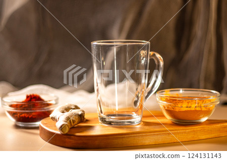 Empty transparent cup on wooden tray with turmeric and chili species. Mock up for design. Served table. Preparation for making drink 124131143