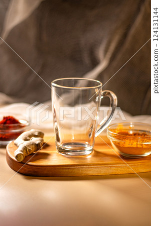 Empty transparent cup on wooden tray with turmeric and chili species. Mock up for design. Served table. Preparation for making drink 124131144