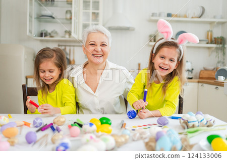 Happy Easter. Two little girls sisters twins grandmother painting eggs enjoying time together. Happy family grandma granddaughters child kids preparing for Easter. Spring Christian festival tradition Happy Easter. Two little girls sisters twins grandmother painting eggs enjoying time together. Happy family grandma granddaughters child kids preparing for Easter. Spring Christian festival tradition 124133006