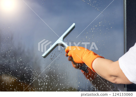 A cleaning lady cleans a window with a scraper. A cleaning lady cleans a window with a scraper. 124133060